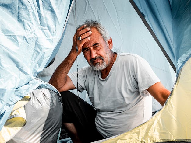 Man met hand op voorhoofd in tent in Griekenland