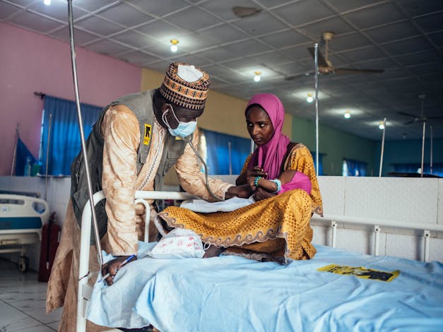 Arts behandeld kind die op schoot van moeder ligt op ziekenhuisbed in Nigeria