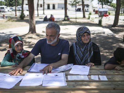 Vrouw en man zitten met hun kinderen achter tafel met daarop documenten om asiel aan te vragen in Duitsland