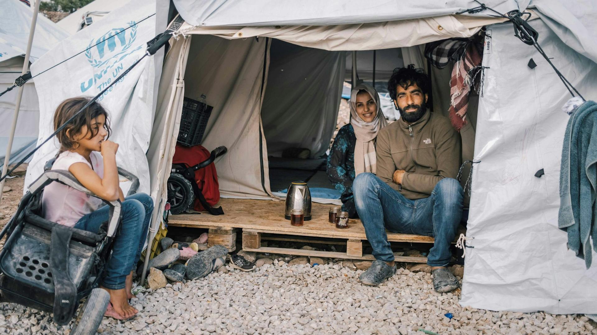 Man en vrouw zitten met kind bij hun tent op een pallet in Griekenland