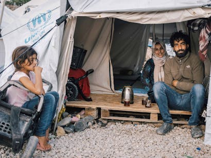 Man en vrouw zitten met kind bij hun tent op een pallet in Griekenland