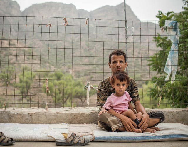 Man zit met dochter op schoot op een matje op de grond in Jemen