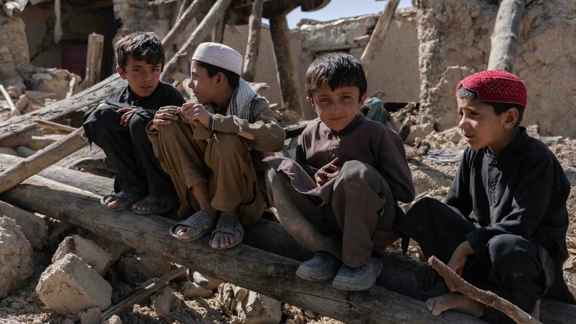 Vier jongens zitten op boomstronk in verwoest gebied in Afghanistan