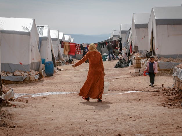 Vrouw loopt met emmer door vluchtelingenkamp