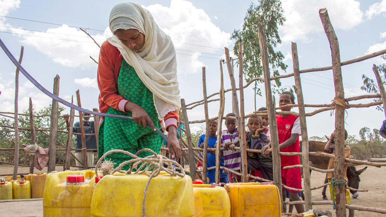 Vrouw vult jerrycans met water in Ethiopië terwijl kinderen toekijken