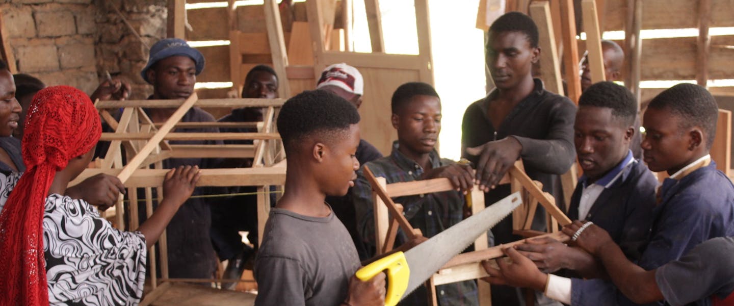 Jongen met zaag in zijn hand met andere leerlingen om hen heen in Congo