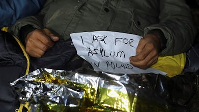 Een migrant houdt poster vast waarin hij vraagt om asiel in Polen