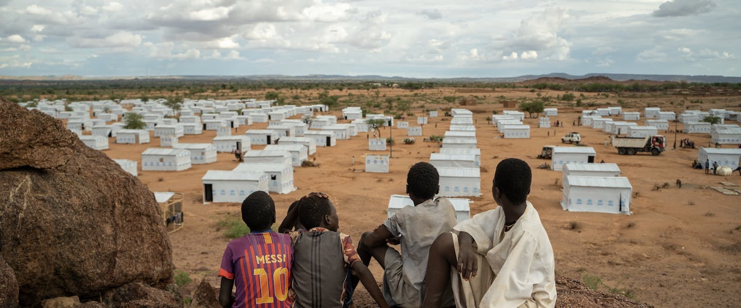 Vier kinderen zitten op uitkijkpunt en kijken uit over vluchtelingenkamp in Tsjaad