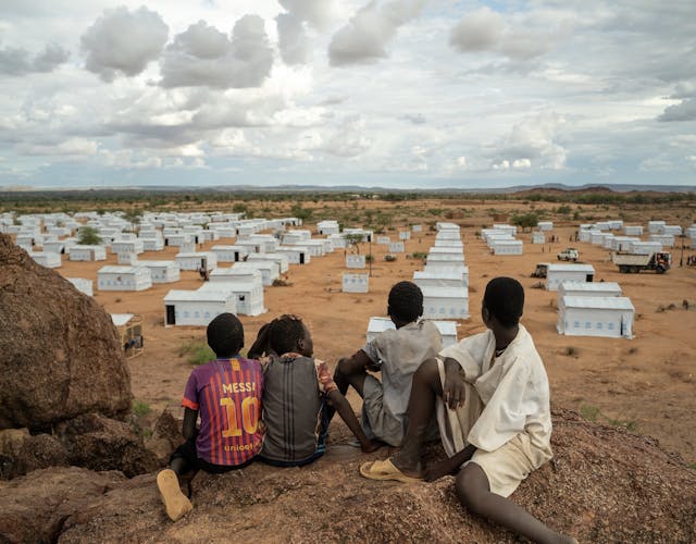 Vier kinderen zitten op uitkijkpunt en kijken uit over vluchtelingenkamp in Tsjaad