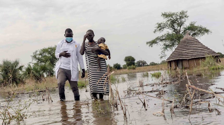 Dokter loopt met moeder en haard kind door overstroomd gebied