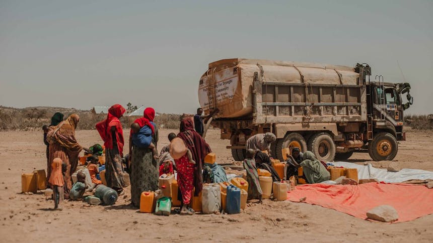 Groep mensen staat bij jerrycans welke volgeladen wordt door truck