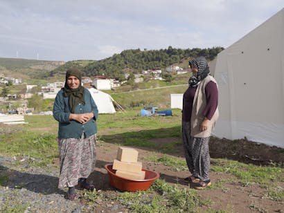 Twee vrouwen met pakketten in bruine bak op de grond voor hun tent