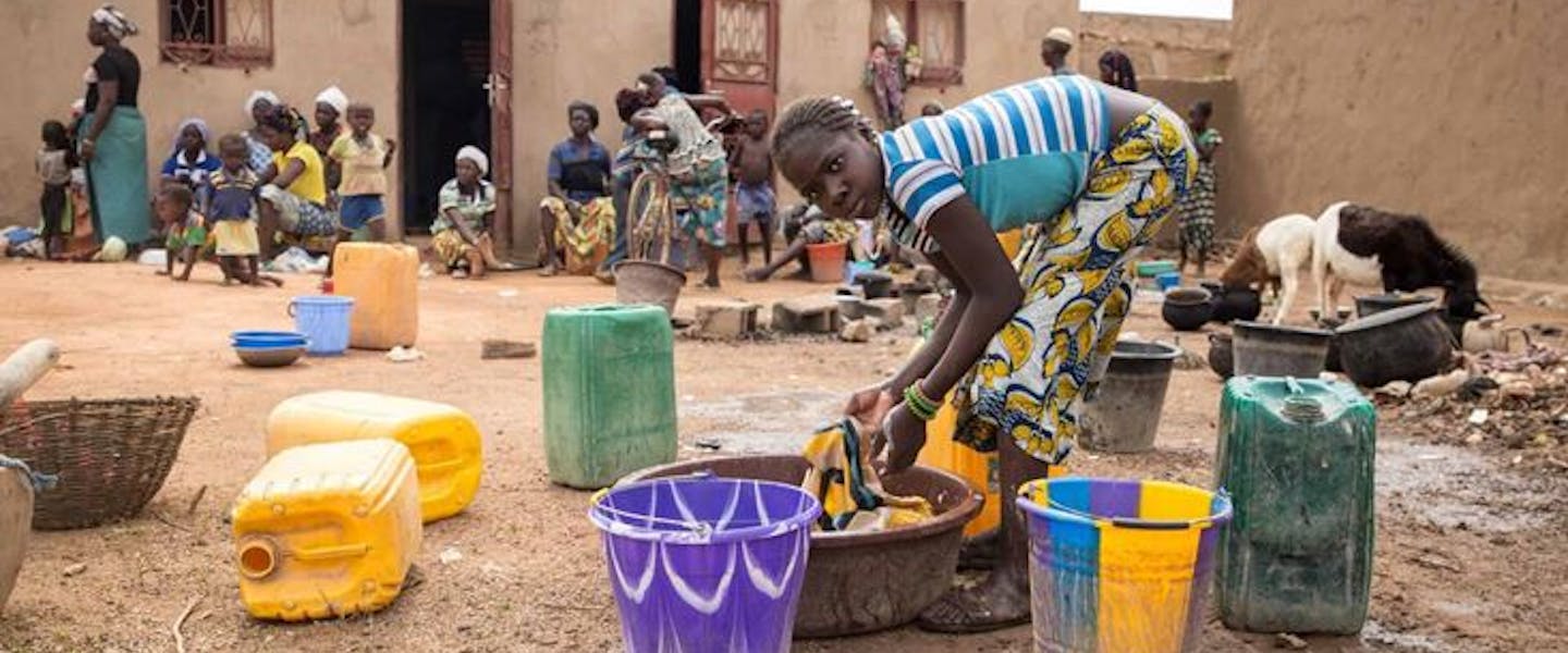 Meisje wast kleren in bruine bak met water in Burkina Faso