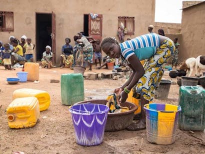 Meisje wast kleren in bruine bak met water in Burkina Faso