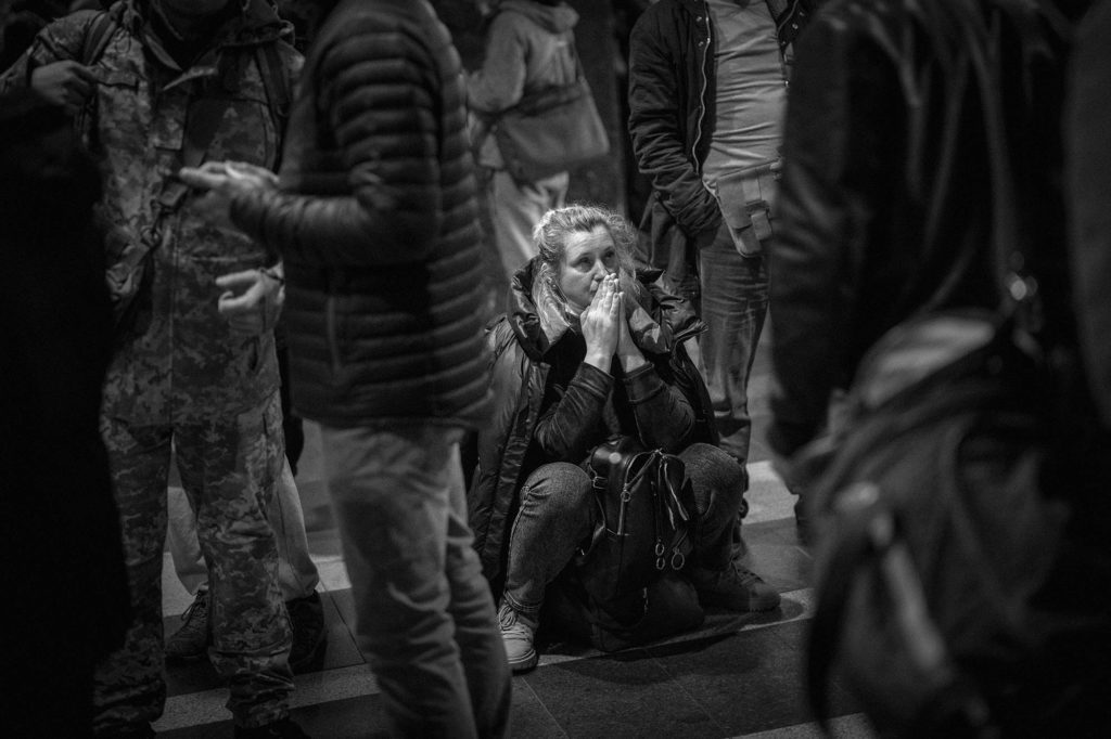 Vrouw hurkt op de grond met handen tegen elkaar voor haar mond en kijkt naar boven