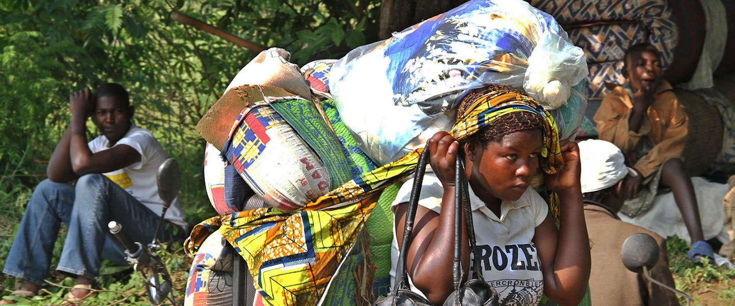 Portretfoto van meisje met zakken met spullen op rug en hoofd en in haar hand