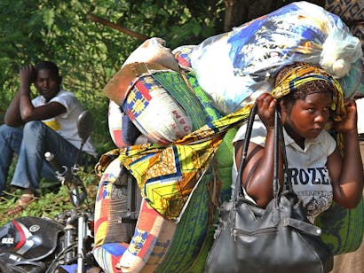 Portretfoto van meisje met zakken met spullen op rug en hoofd en in haar hand