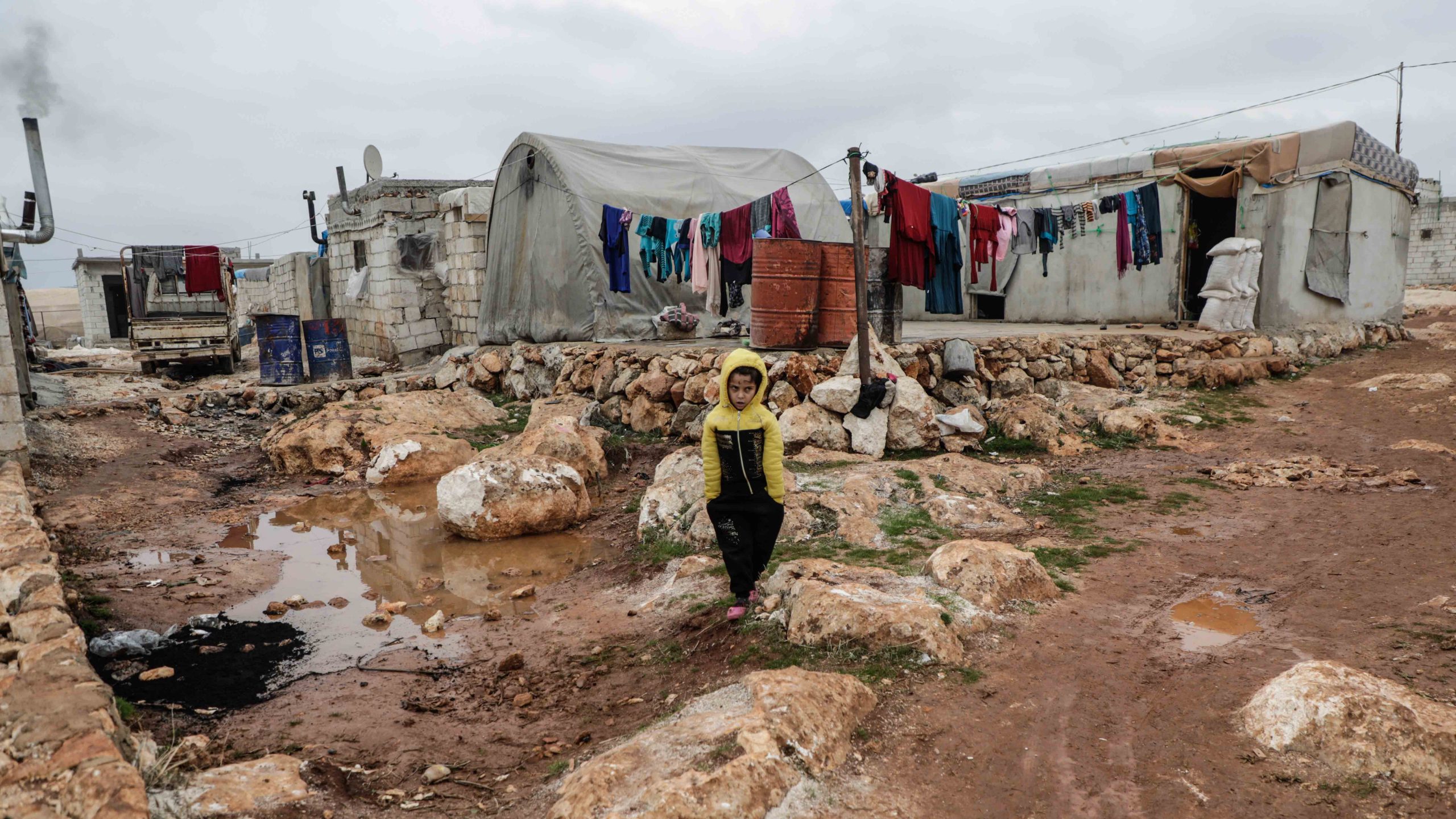 Een jongen staat in een vluchtelingenkamp in de kou in Syrië