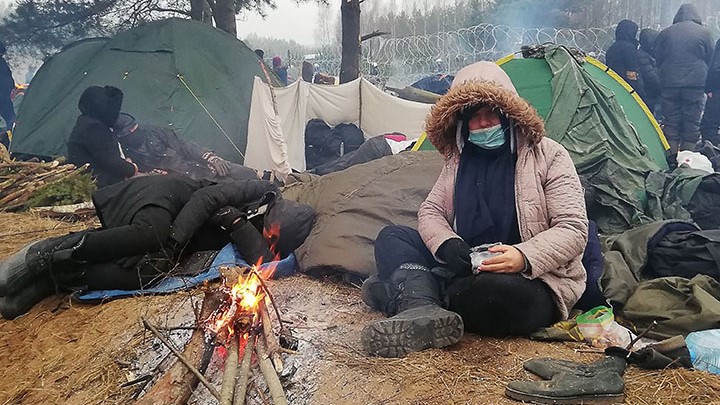 Migrant zit voor tent bij kampvuur bij de Poolse en Wit Russische grens