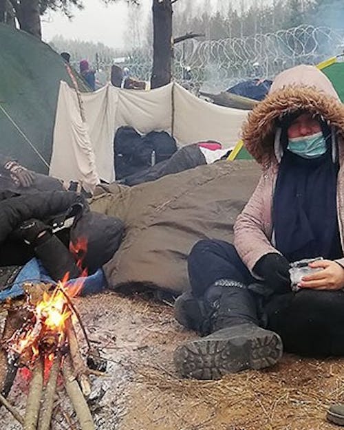 Migrant zit voor tent bij kampvuur bij de Poolse en Wit Russische grens