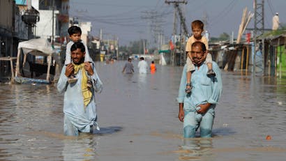 Twee mannen met kinderen op hun schouders lopen door overstroomd gebied