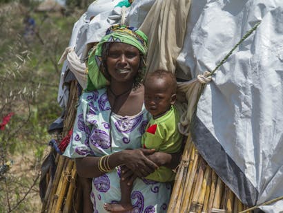 Vrouw staat in de ingang van haar hut met kind in haar armen