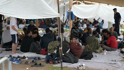Vluchtelingen zitten op kleden in Ter Apel