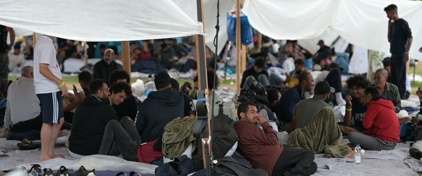 Vluchtelingen zitten op kleden in Ter Apel