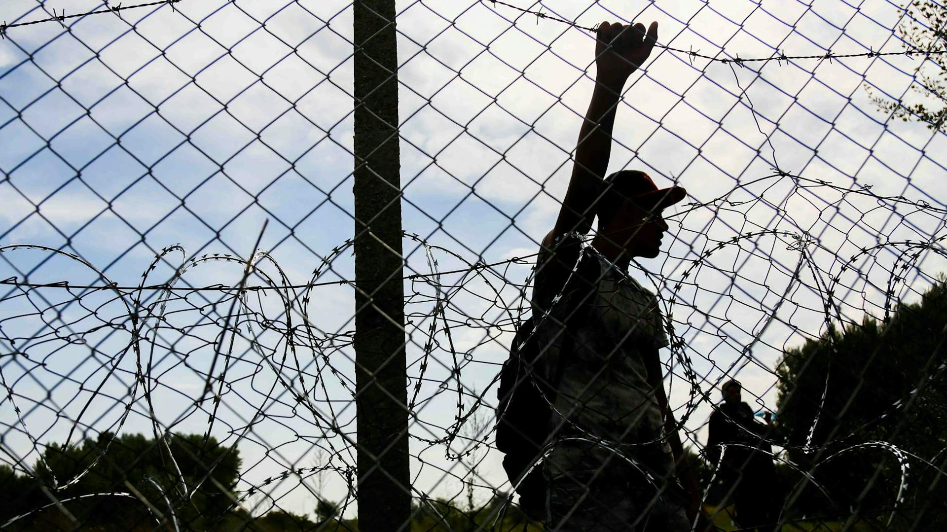 Persoon op de vlucht staat achter prikkeldraad van hek aan de Hongaarse grens.
