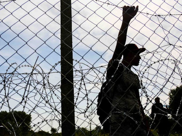 Persoon op de vlucht staat achter prikkeldraad van hek aan de Hongaarse grens.