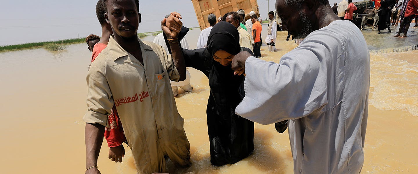 Twee mannen helpen een vrouw door het overstroomde gebied heen in Soedan