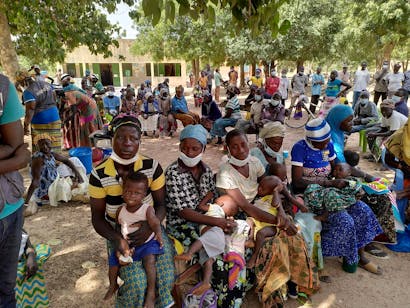 Groep mensen zitten met hun baby's op hun schoot in Burkina Faso