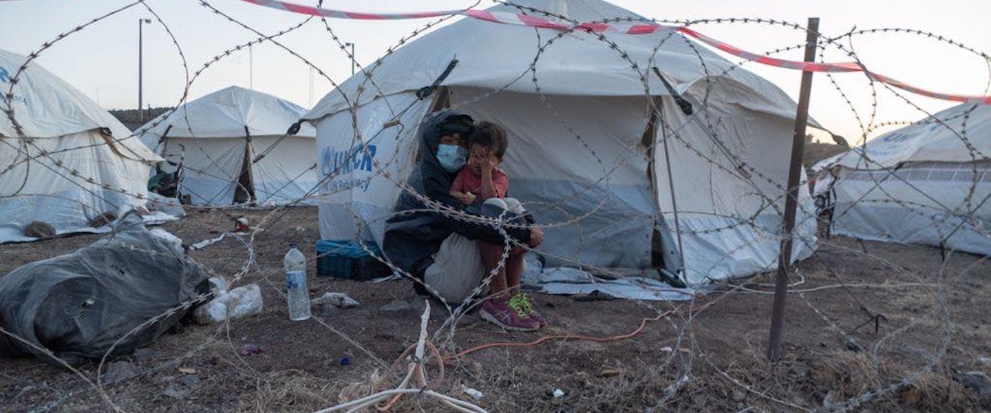 Moeder houdt kind vast achter prikkeldraad in vluchtelingenkamp