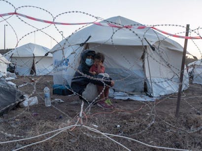 Moeder houdt kind vast achter prikkeldraad in vluchtelingenkamp