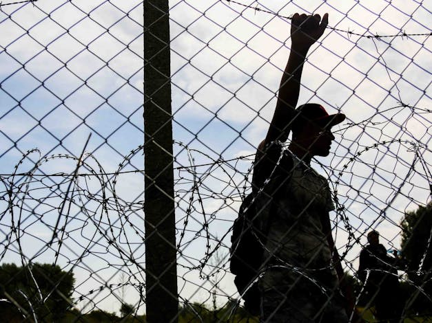 Man staat achter hek met prikkeldraad bij de Hongaarse grens