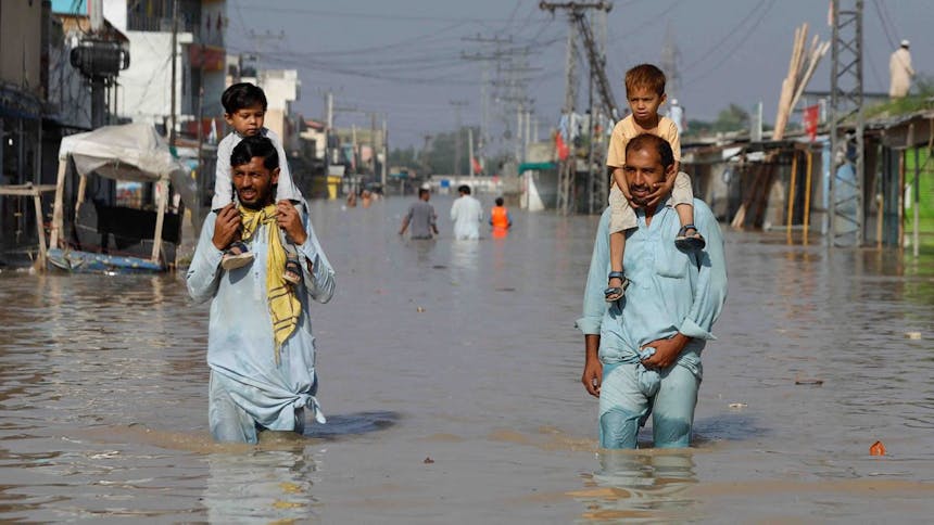 Twee mannen lopen met allebei een kind op hun schouders door het overstroomde gebied in Pakistan