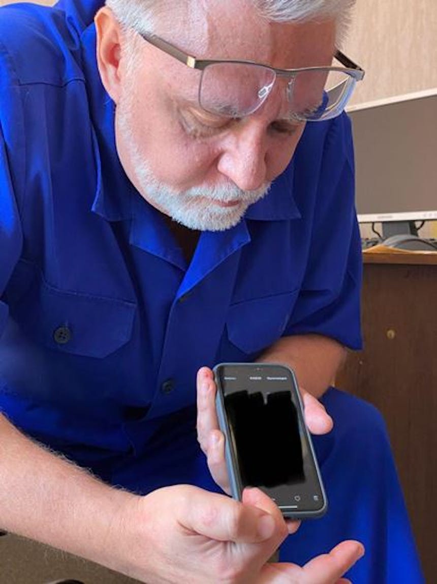 Foto van man met blauwe kleding die zijn telefoon laat zien