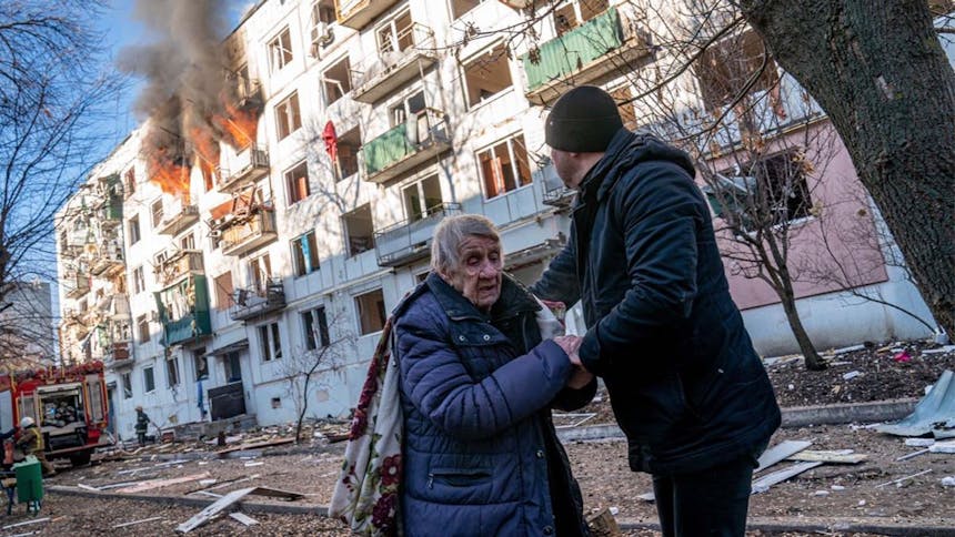 Man houdt oudere vrouw vast met brandend gebouw op de achtergrond