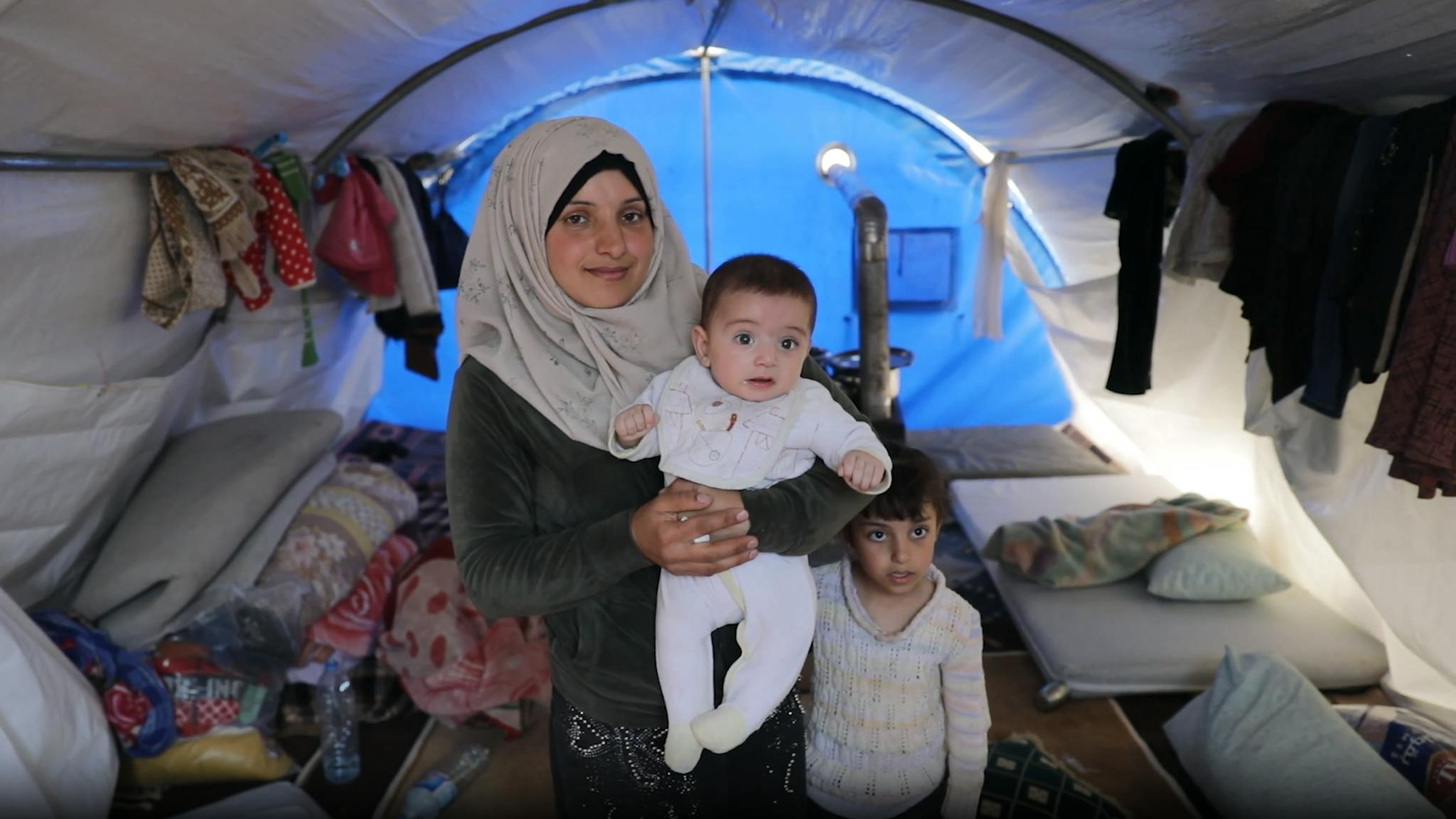 Vrouw met baby kijkt camera in terwijl ze in tent staat