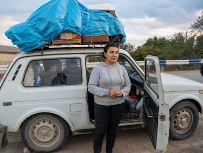 mensen staan voor een witte auto waarin ze gevlucht zijn uit Nagorno-Karabach