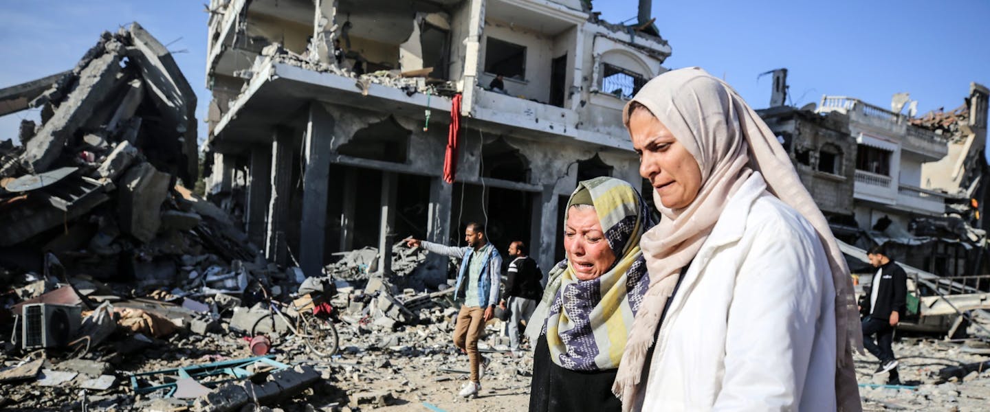 vrouwen staan bedroefd voor een kapot gebouw in gaza