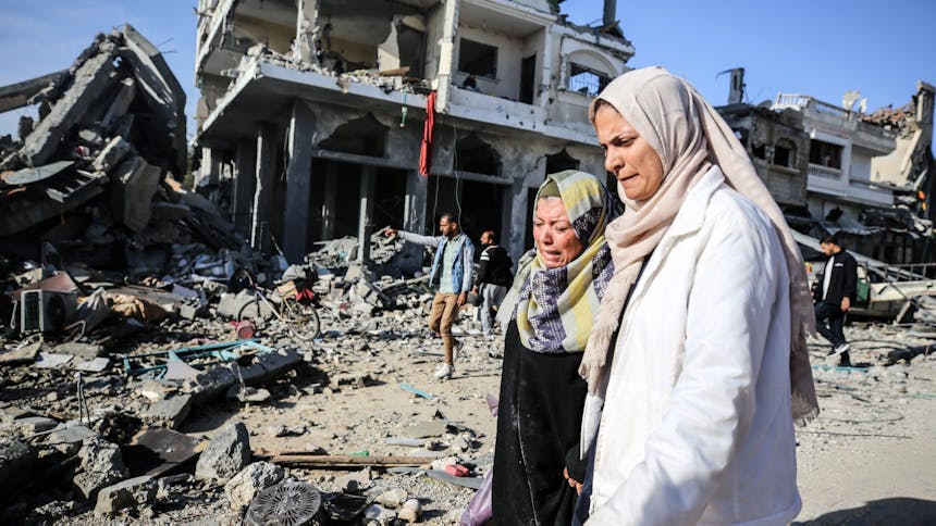 vrouwen staan bedroefd voor een kapot gebouw in gaza