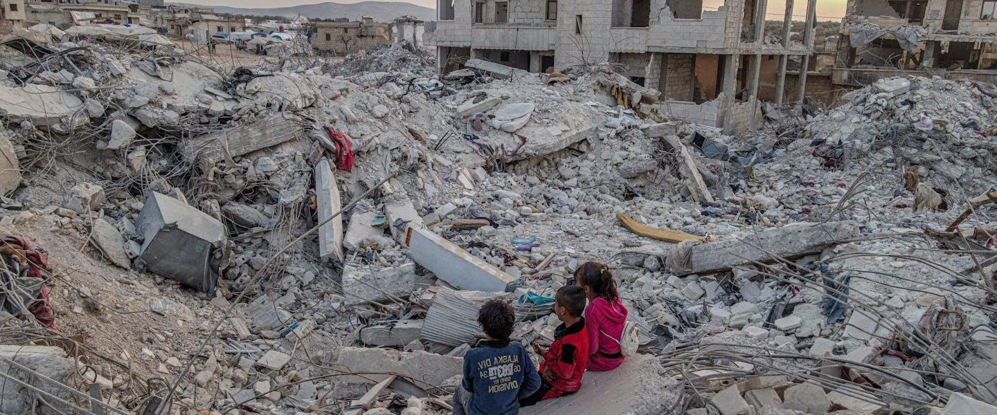 kinderen zitten op door aardbeving verwoeste gebouwen in Syrie