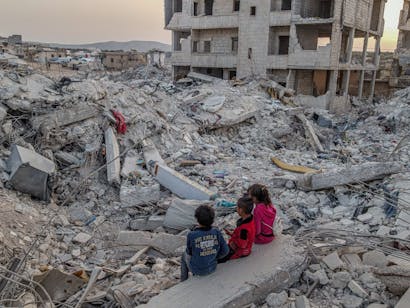 kinderen zitten op door aardbeving verwoeste gebouwen in Syrie