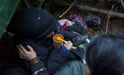 mensen op de vlucht met dikke jassen eten soep aan de pools-belarussische grens