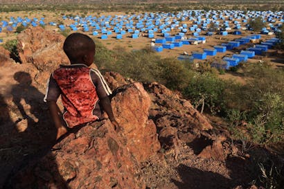 een jongetje zit op een heuvel en kijkt uit over een vluchtelingenkamp bij de Soedanese grens.