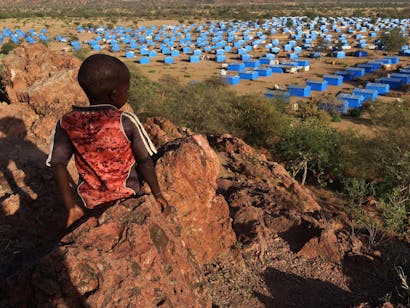 een jongetje zit op een heuvel en kijkt uit over een vluchtelingenkamp bij de Soedanese grens.