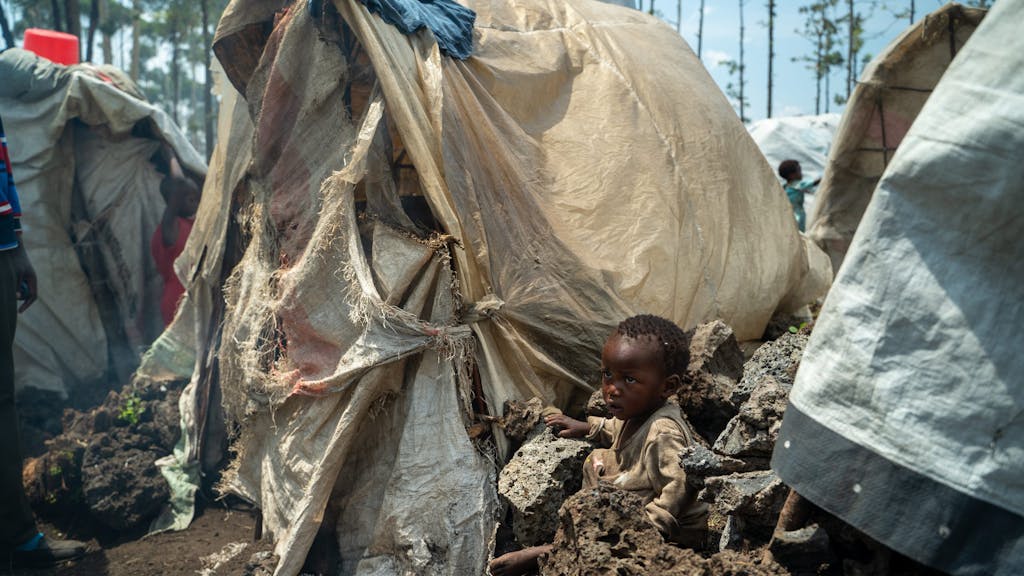 een jongetje zit naast een tent in een vluchtelingenkamp bij Goma.