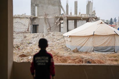 Een kind kijkt naar een tent en ingestorte gebouwen in Syrië