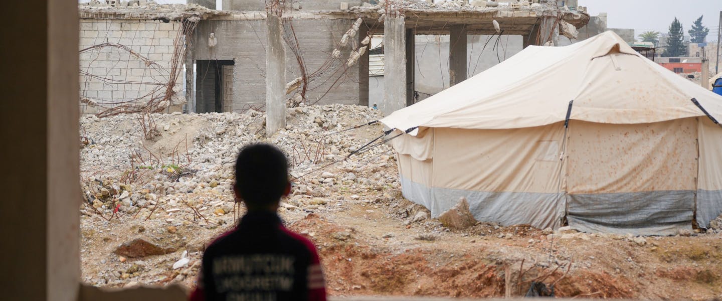 Een kind kijkt naar een tent en ingestorte gebouwen in Syrië